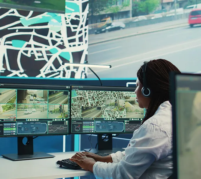 Woman with headset monitors traffic camera feeds and street maps on dual computer screens.