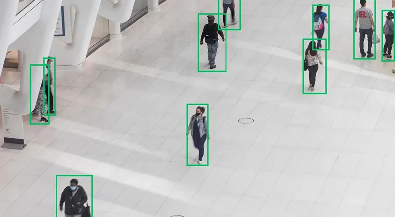 People walking inside a large indoor area with green boxes highlighting each individual.