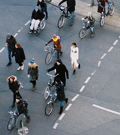 Group of people walking and riding bikes on a city street, including a person in a wheelchair.
