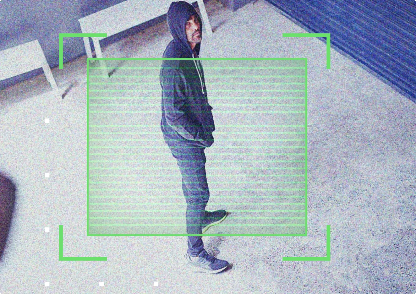 Man in dark hoodie and pants standing with hands in pockets on a concrete floor.
