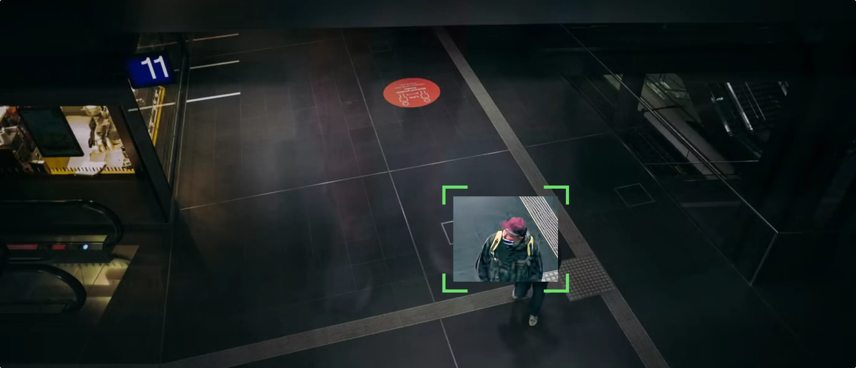 Surveillance camera view of person walking indoors wearing a mask, red cap, and backpack.
