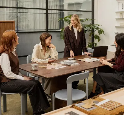Four women having a friendly meeting sitting around a table with papers and laptops in a modern office.