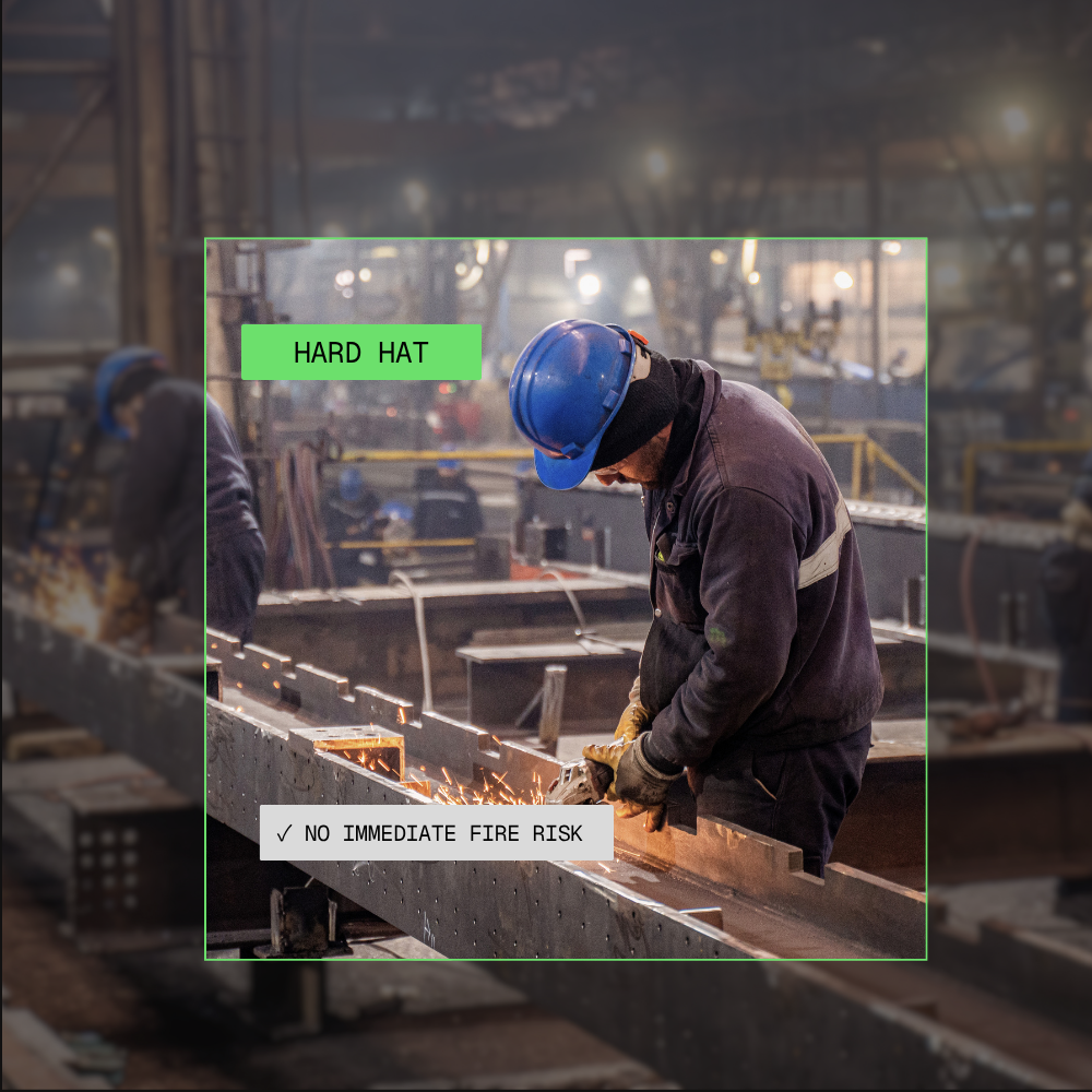 Worker in a factory wearing a blue hard hat and gloves while grinding metal with sparks flying.