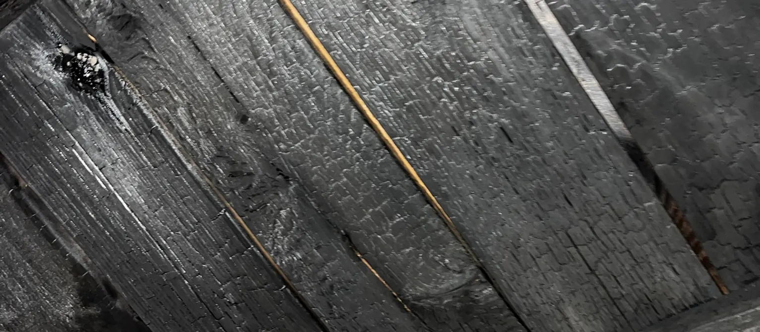 Close view of fire-blackened roof boards and a charred beam