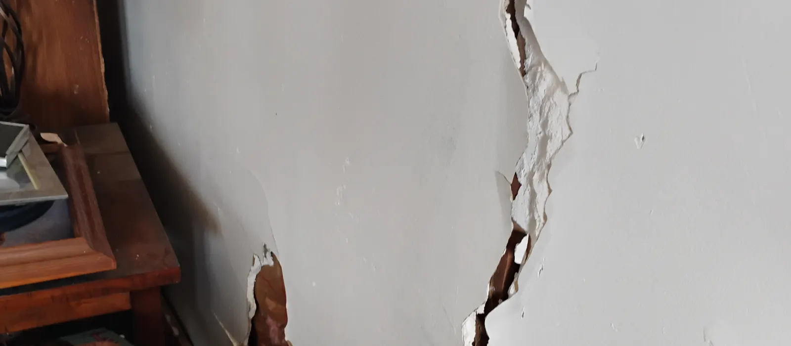 Wide crack running down a living room wall beside a wooden side table