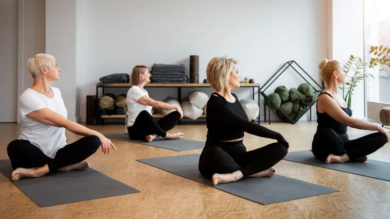 Four people in a yoga class are seated on mats, twisting their torsos while looking sideways.