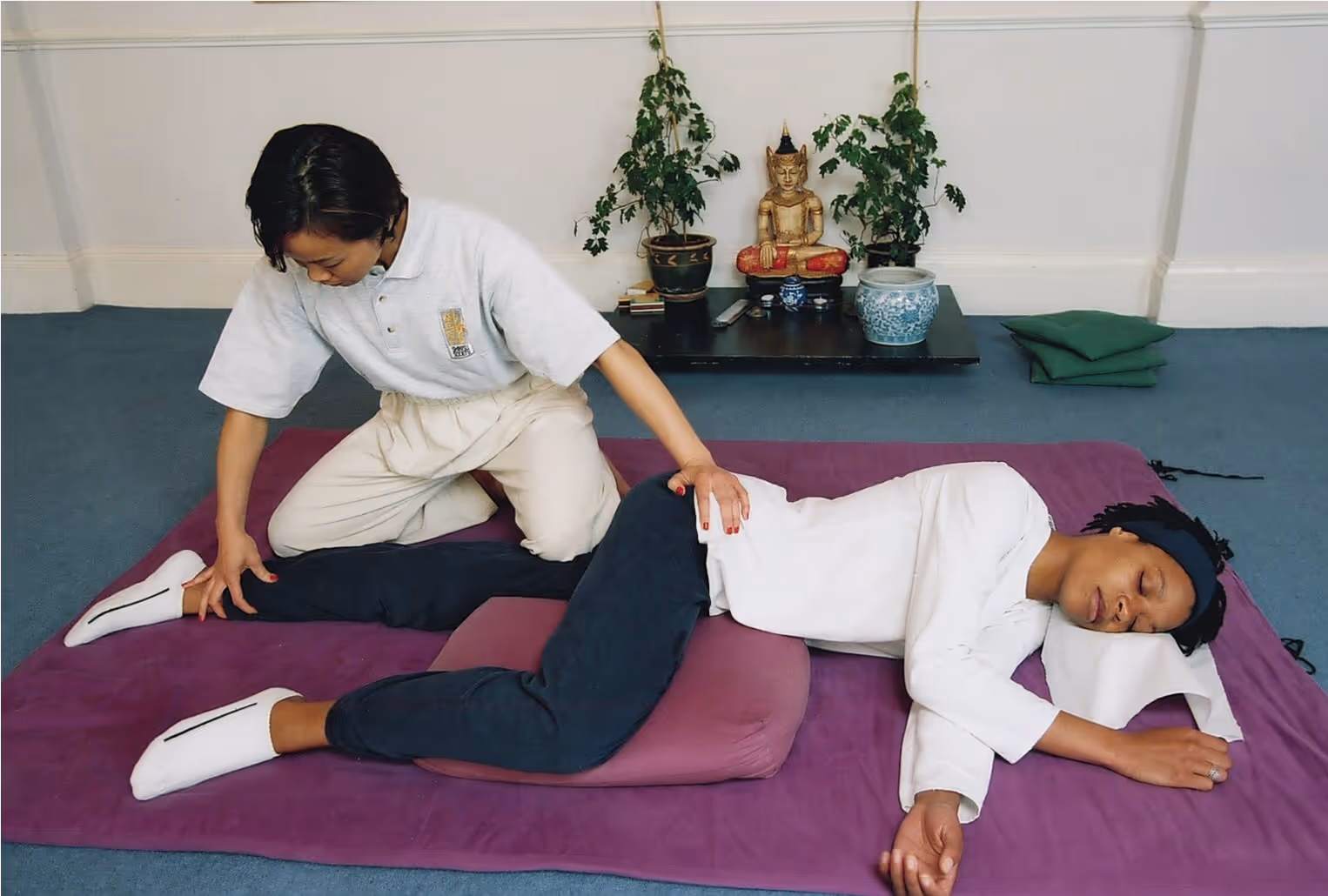 A person gives a massage to another person lying on their side on a mat.
