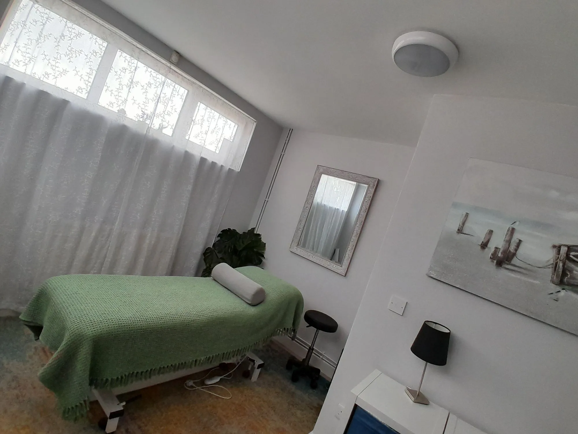 A massage table with a green blanket and pillow in a bright room.