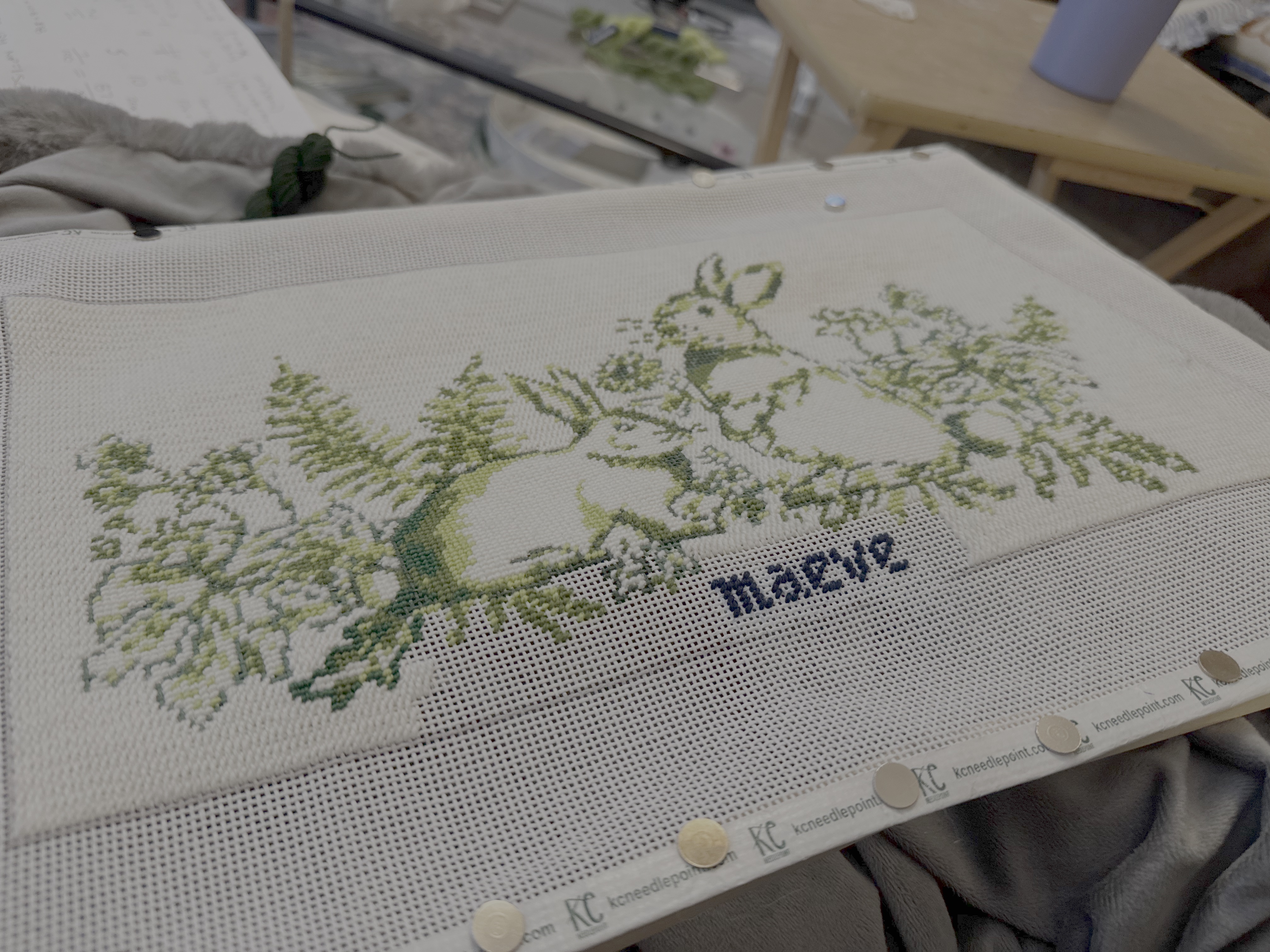Cross-stitch embroidery of two rabbits surrounded by flowers with the name Maeve stitched below.
