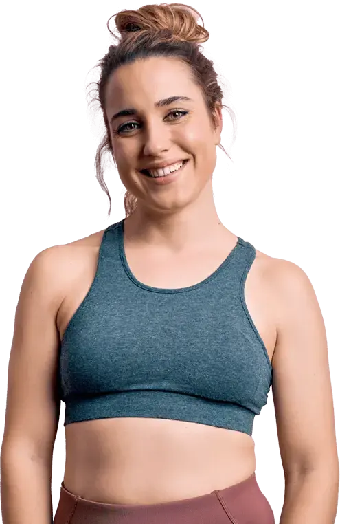 Smiling woman in a blue sports bra and light brown leggings with a hair bun.