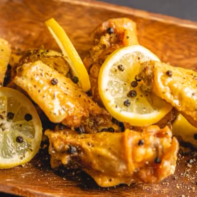 Fried chicken wings garnished with lemon slices and black pepper on a wooden plate.
