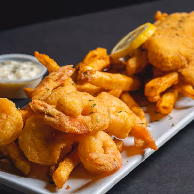Plate of crispy fried shrimp, fries, hush puppies, and a lemon wedge with dipping sauce on the side.