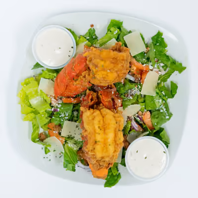 Salad with lettuce, tomato, cheese, two fried pieces of fish, and two cups of ranch dressing.