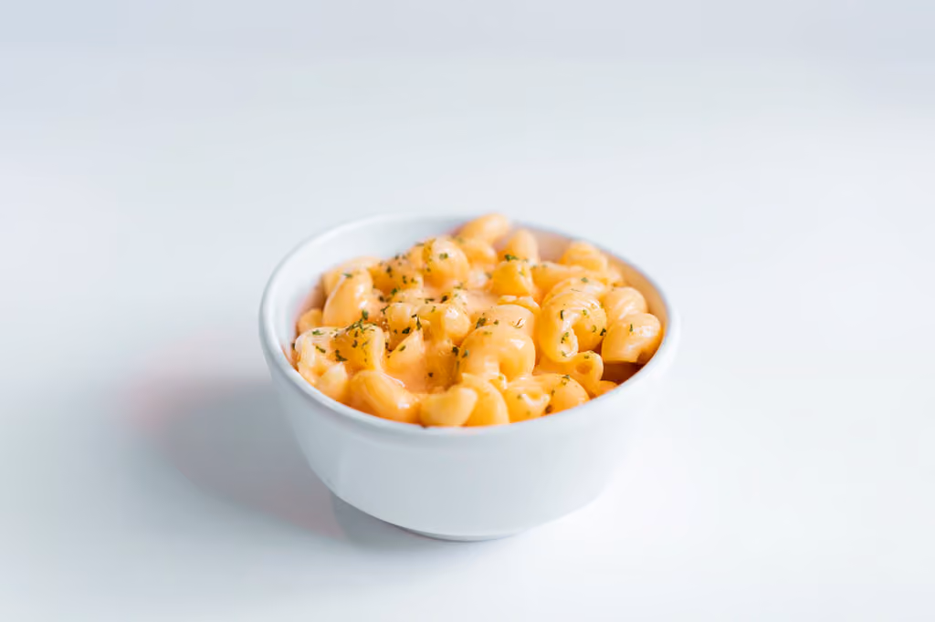 White bowl of creamy macaroni and cheese garnished with herbs on a white surface.
