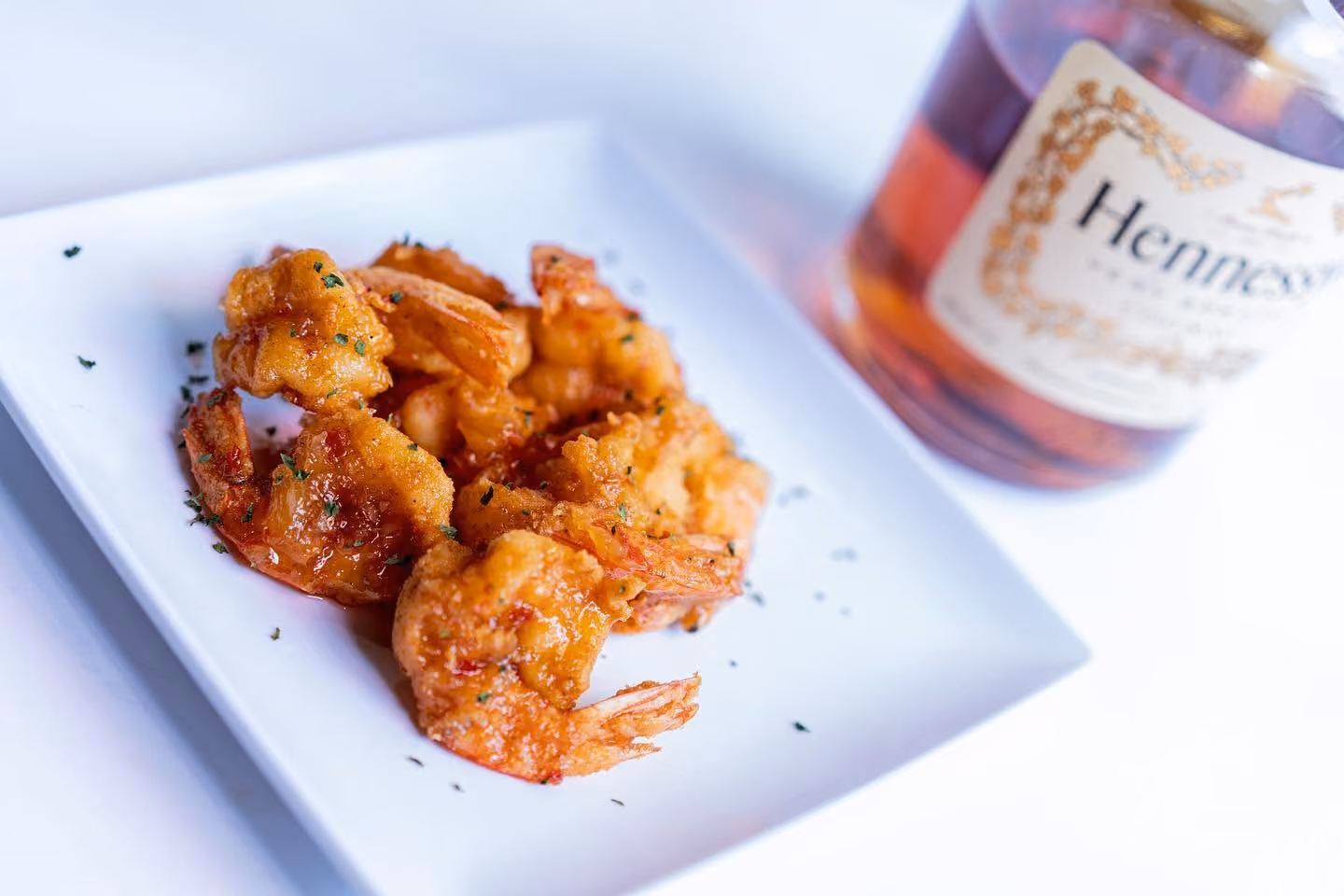 A plate of shrimp with a bottle of whiskey behind it.