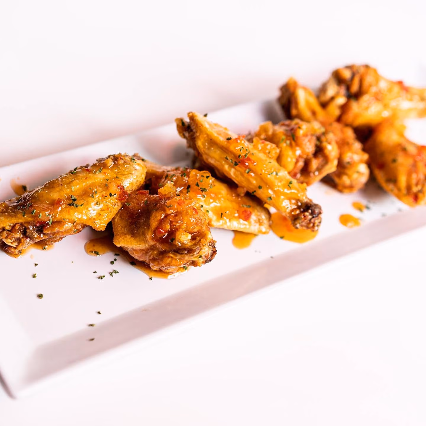 Plate of glazed chicken wings garnished with herbs on a white rectangular dish.