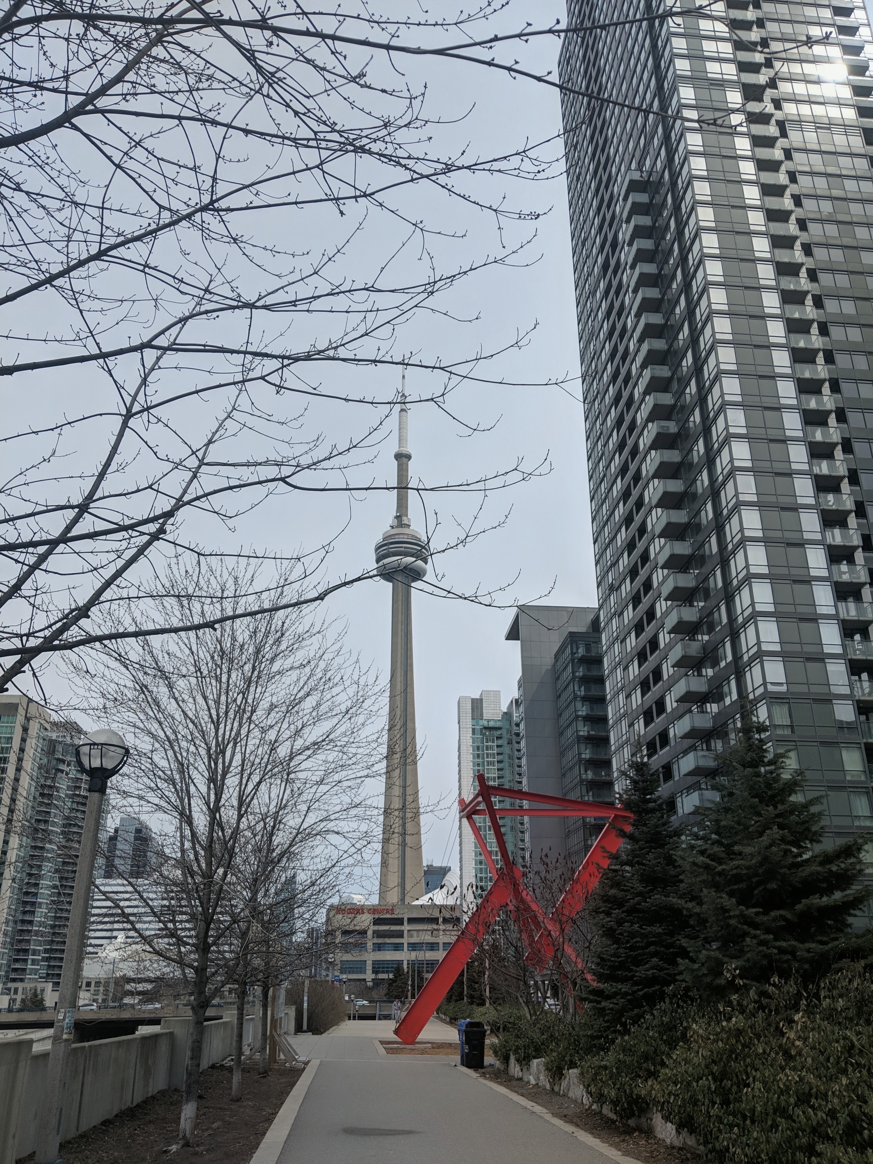 Tree-lined walkway beside CityPlace condo towers, with the CN Tower in the distance