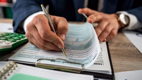 Person filling out a 1040 tax form with a pen on a clipboard at a wooden desk.