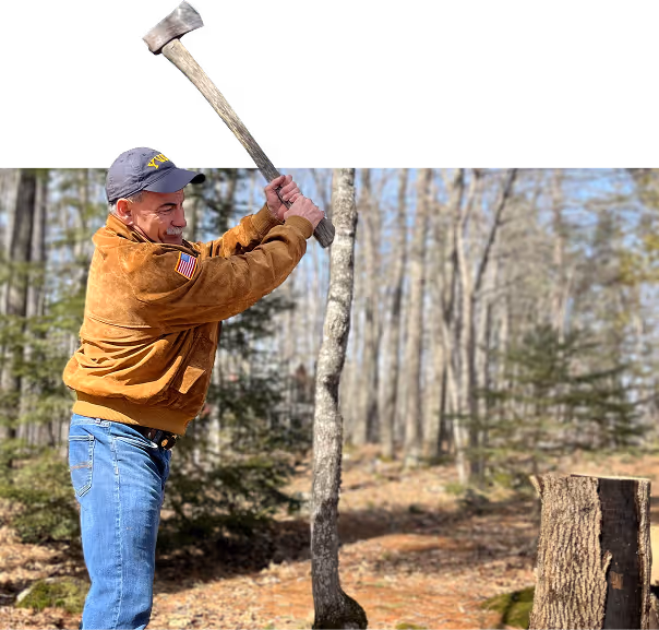 Man in brown jacket and cap swinging an axe to chop a tree in a forest.