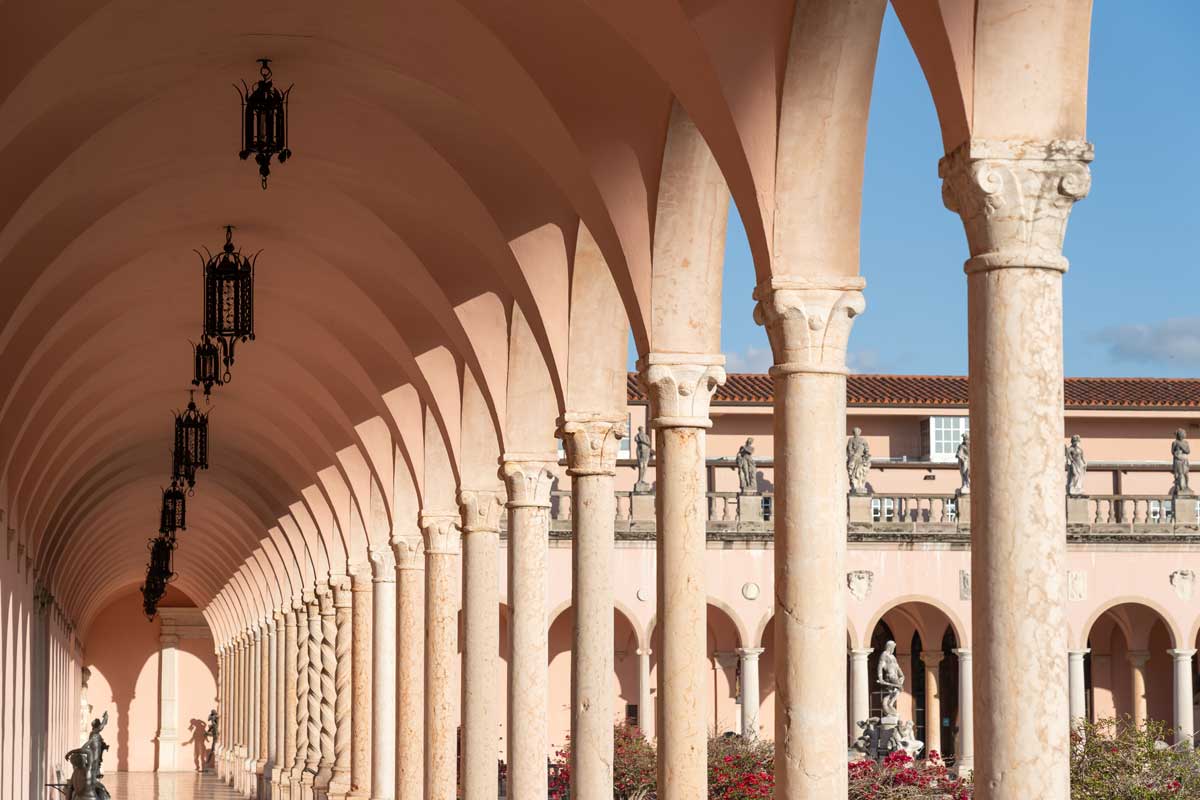 Arched colonnade with ornate columns and hanging lanterns under a clear blue sky.