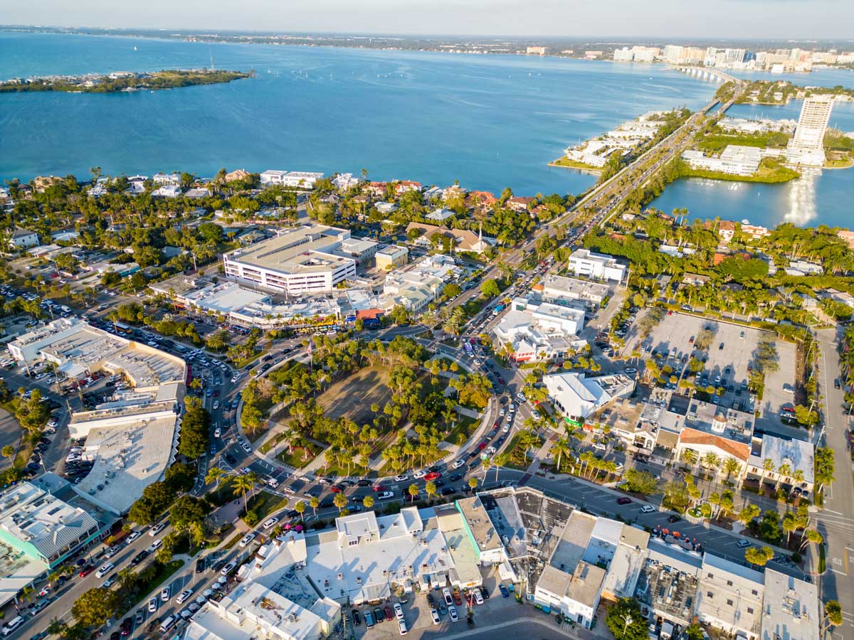 Aerial view of a coastal city with roundabout, buildings, roads, and blue water in the background.