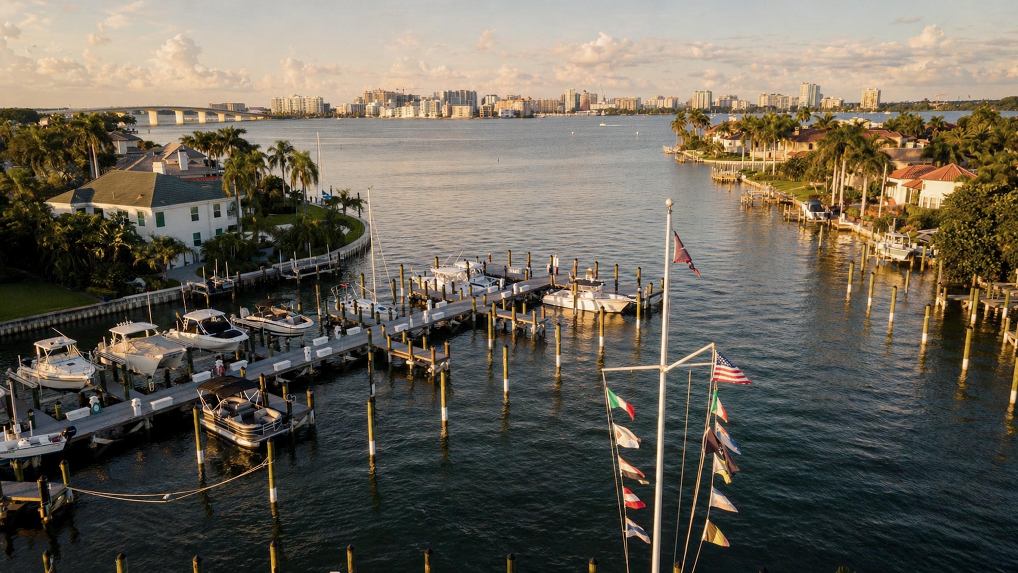 Marina with boats docked along piers and waterfront homes under a cloudy sky at sunset.