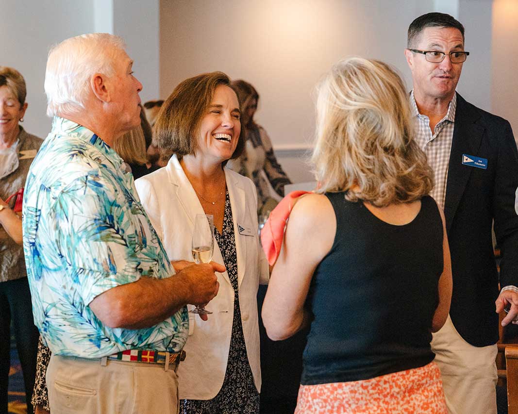 Four adults engaged in conversation at an indoor social event, one holding a glass of wine.