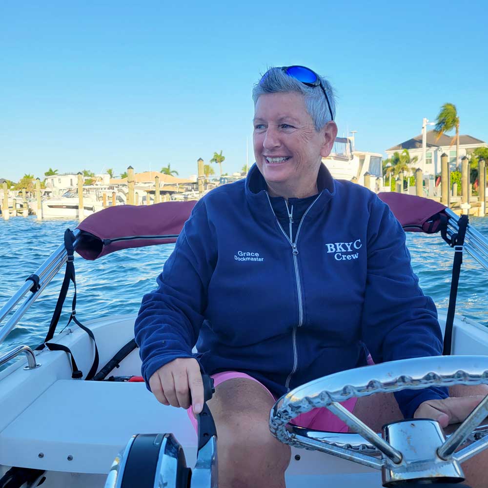 Person steering a boat, wearing a navy BKYC Crew jacket and sunglasses on their head.