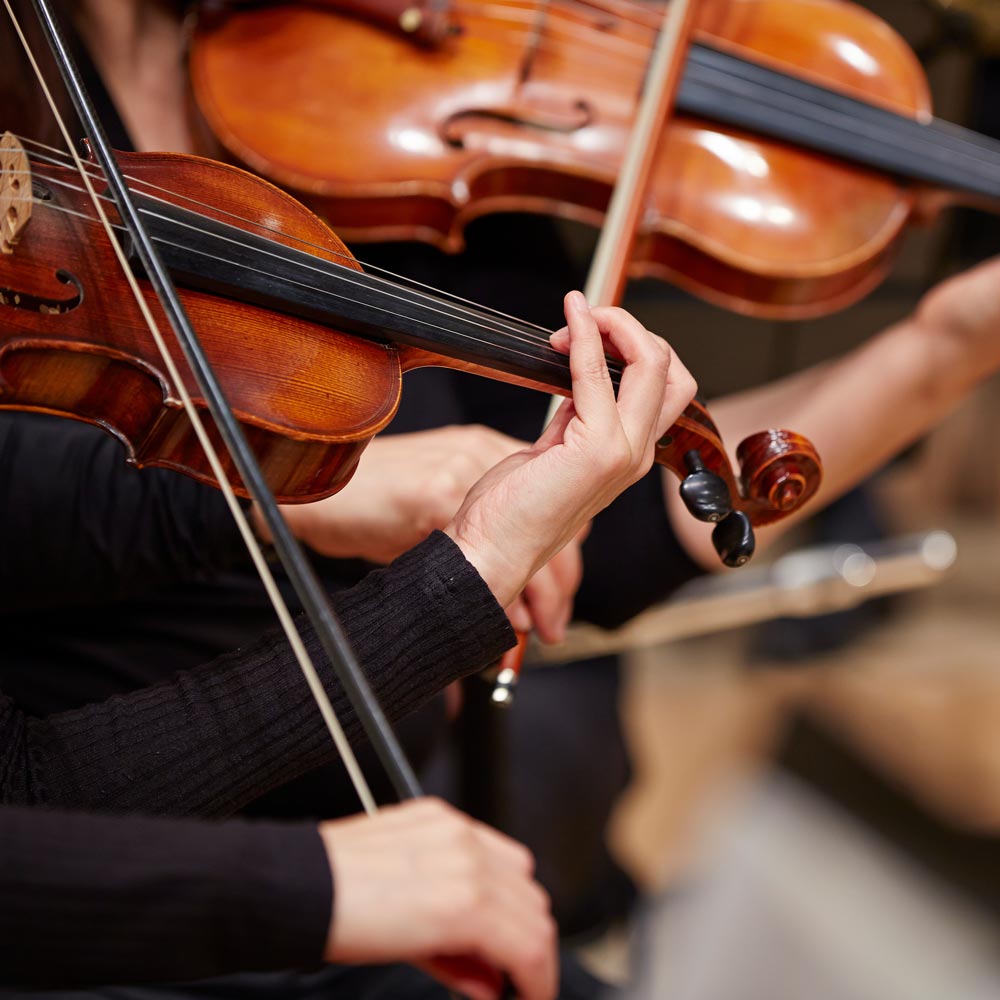 Close-up of hands playing violins in a string orchestra performance.