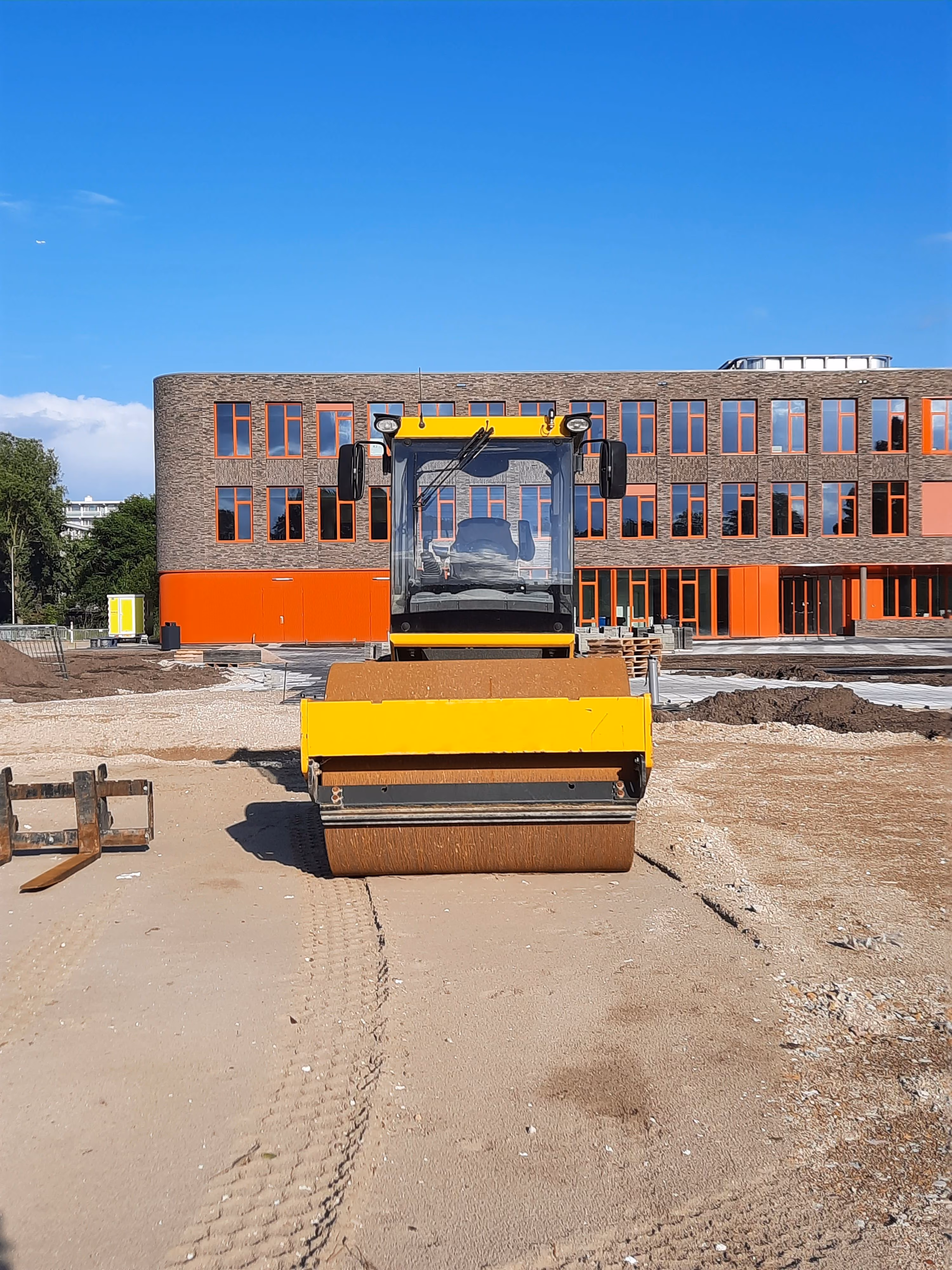 Wals verdicht het zandbed voor een nieuw schoolgebouw, tijdens het bouwrijp maken van het terrein