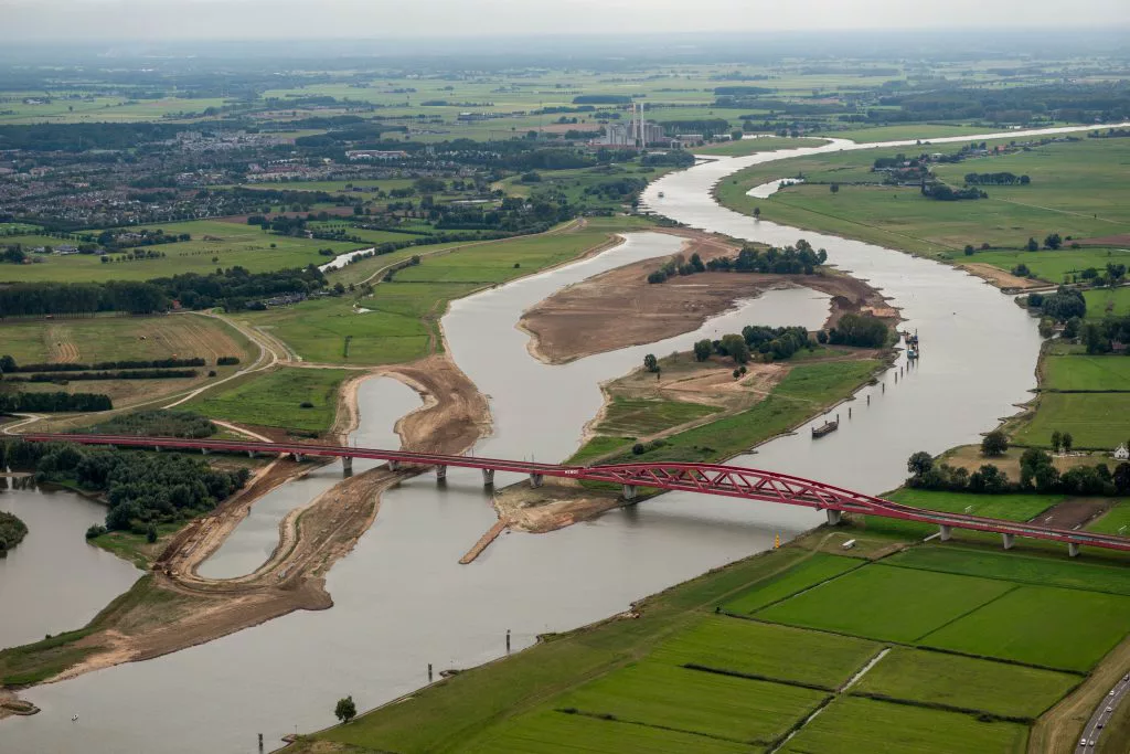 Luchtfoto van een rivier met nevengeul, uiterwaarden en een spoorbrug