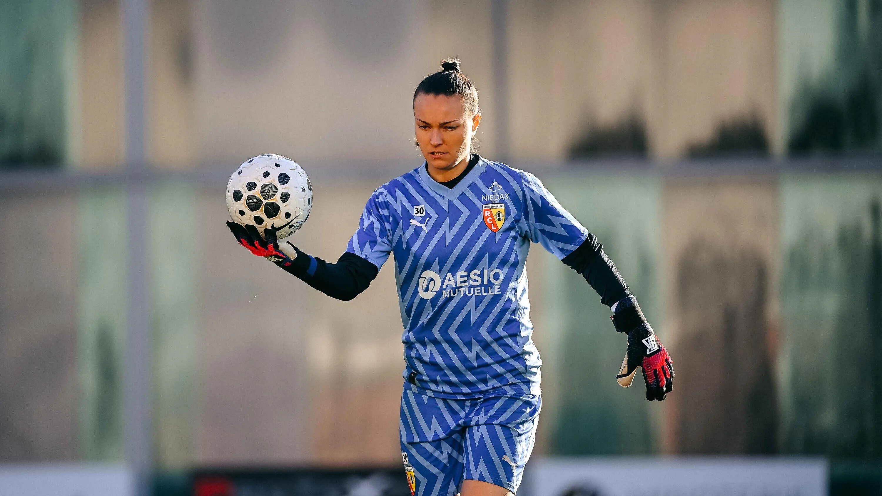Gardienne de but en maillot bleu tenant un ballon de football d'une main gantée.