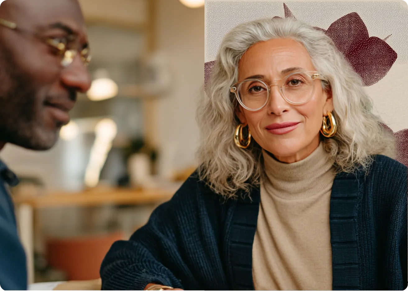 Une femme aux cheveux gris et lunettes souriant, discutant avec un homme en arrière-plan flou.