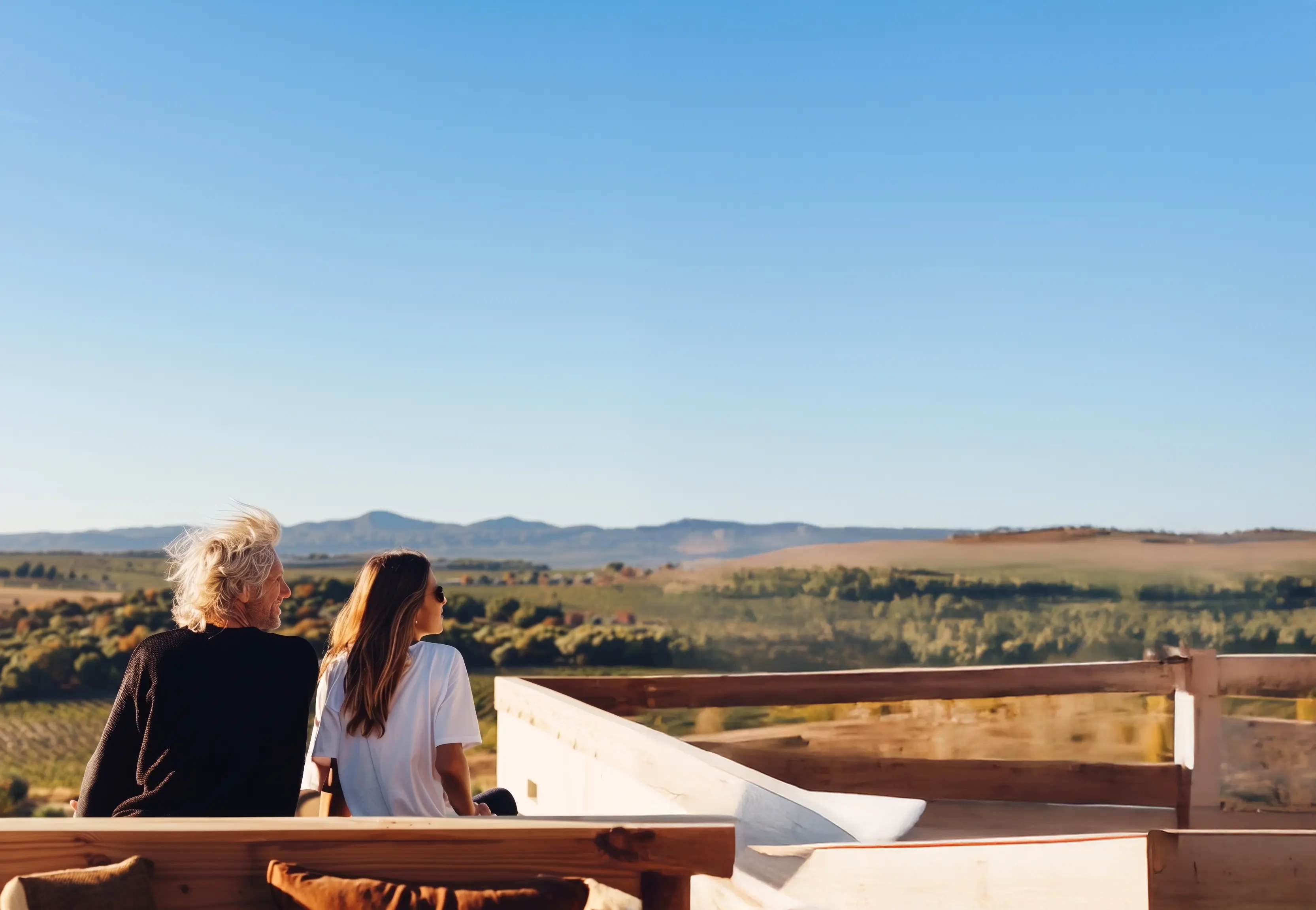 Un homme et une femme regardent un paysage rural vallonné sous un ciel bleu clair.