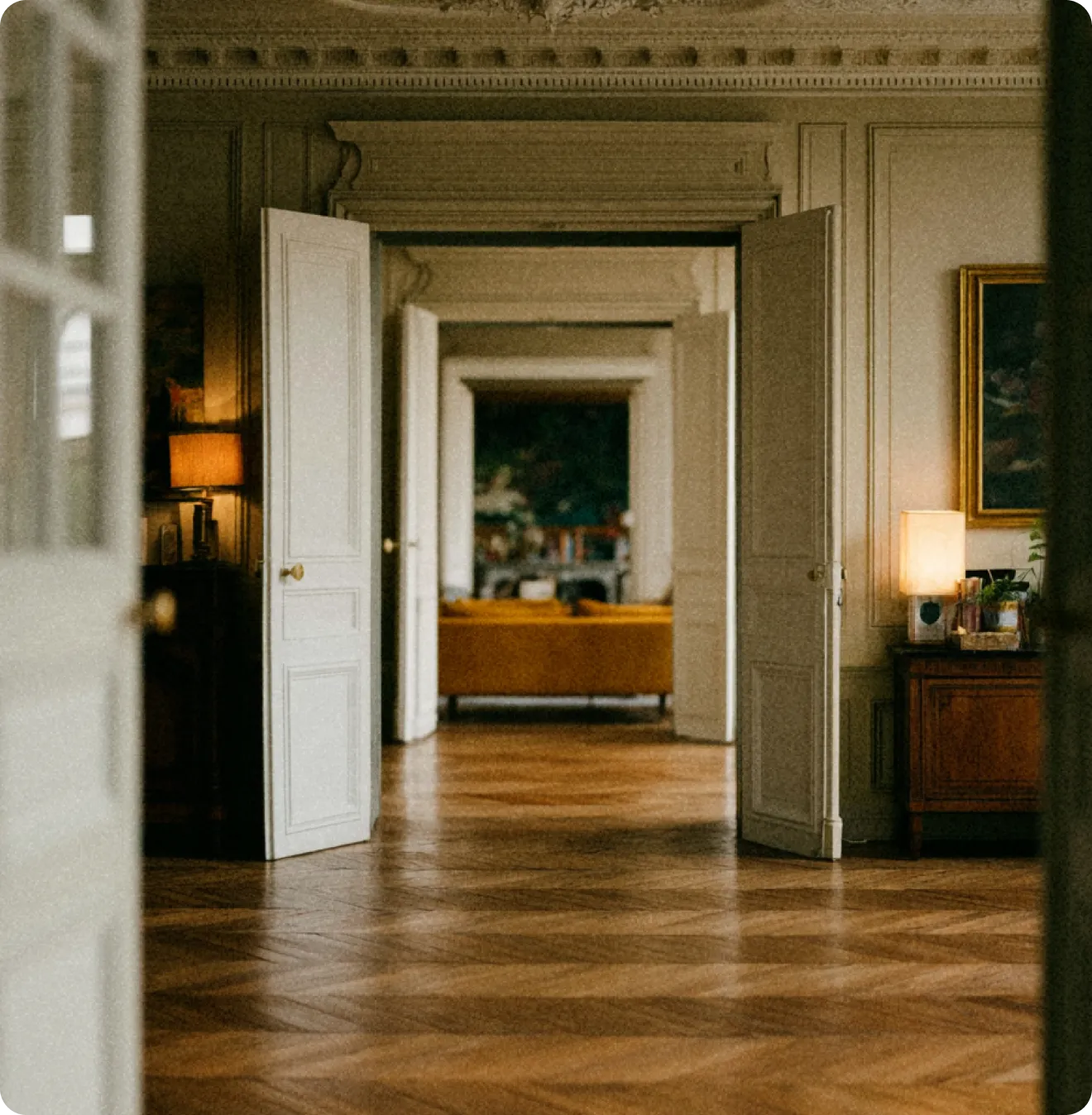 Série de portes blanches ouvertes dans une pièce élégante avec parquet et canapé jaune visible au loin.