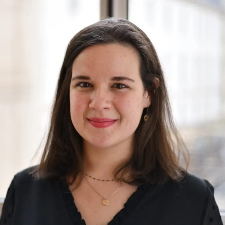 Portrait d'une femme souriante aux cheveux bruns, portant une blouse noire et des bijoux dorés.