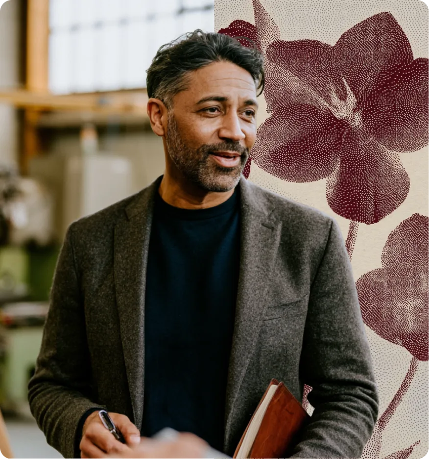 Homme mûr souriant, tenant un carnet, en veste grise, devant un mur à motif floral rouge.
