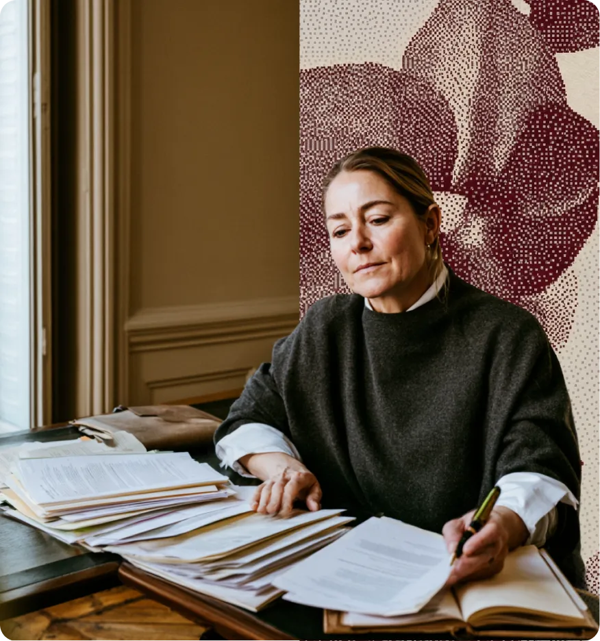Femme examinant des documents papier sur une table en bois dans une pièce au décor classique.