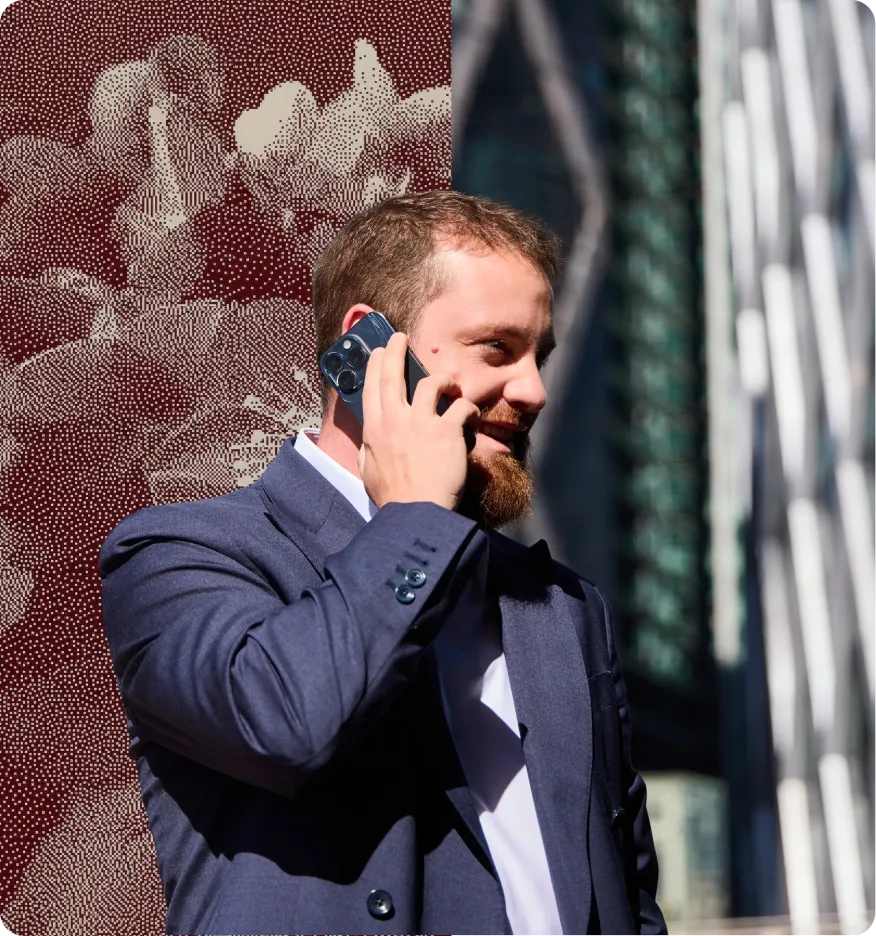 Un homme barbu en costume parle au téléphone avec des gratte-ciels en arrière-plan.