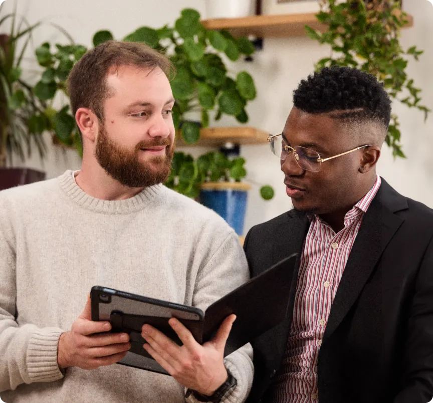 Deux hommes regardent une tablette ensemble dans un bureau avec des plantes en arrière-plan.