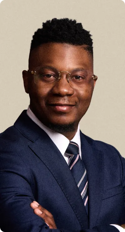Homme d'affaires portant un costume bleu marine et une cravate rayée, bras croisés, souriant.