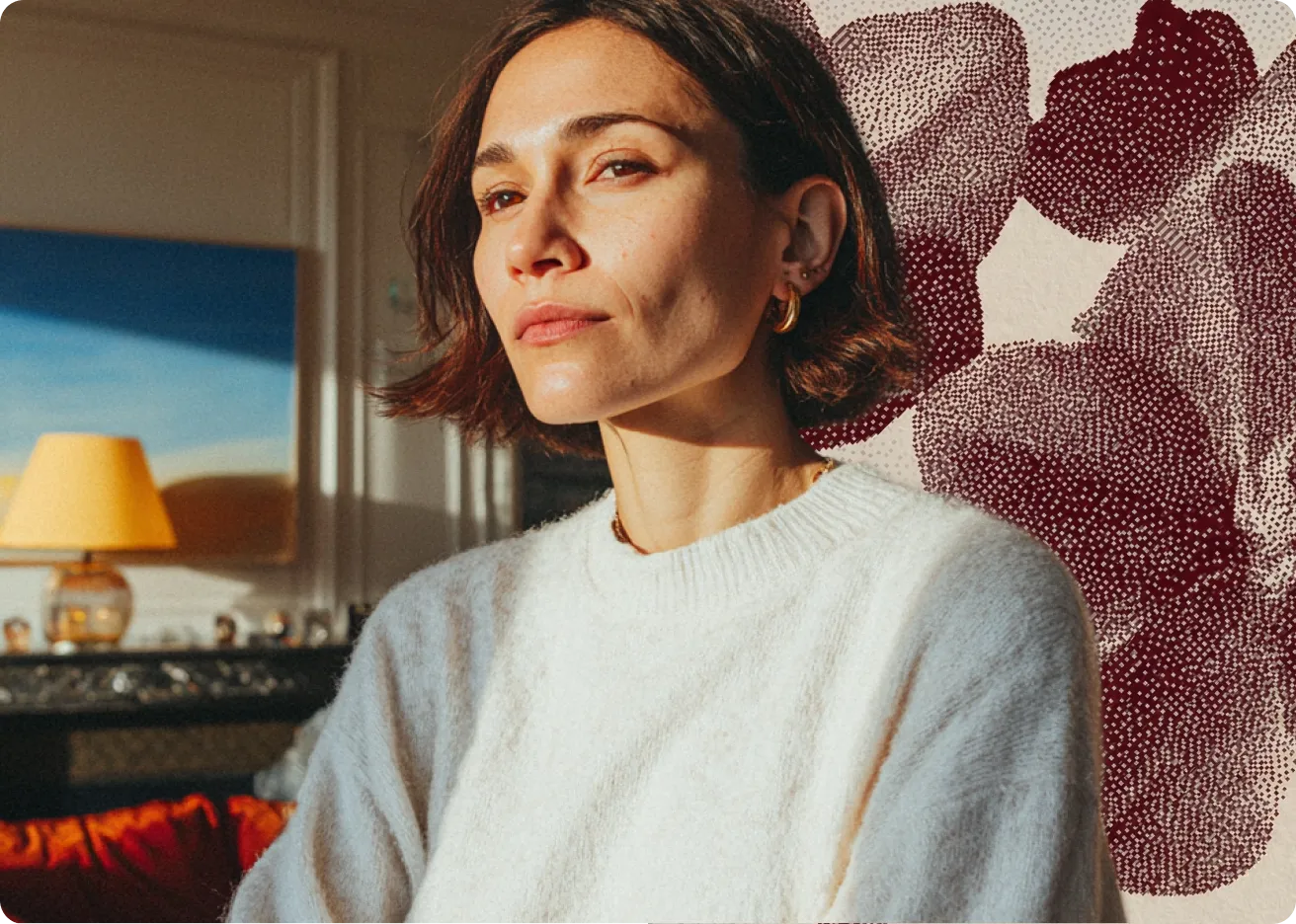 Femme aux cheveux courts portant un pull blanc, posant devant un mur avec décor abstrait.
