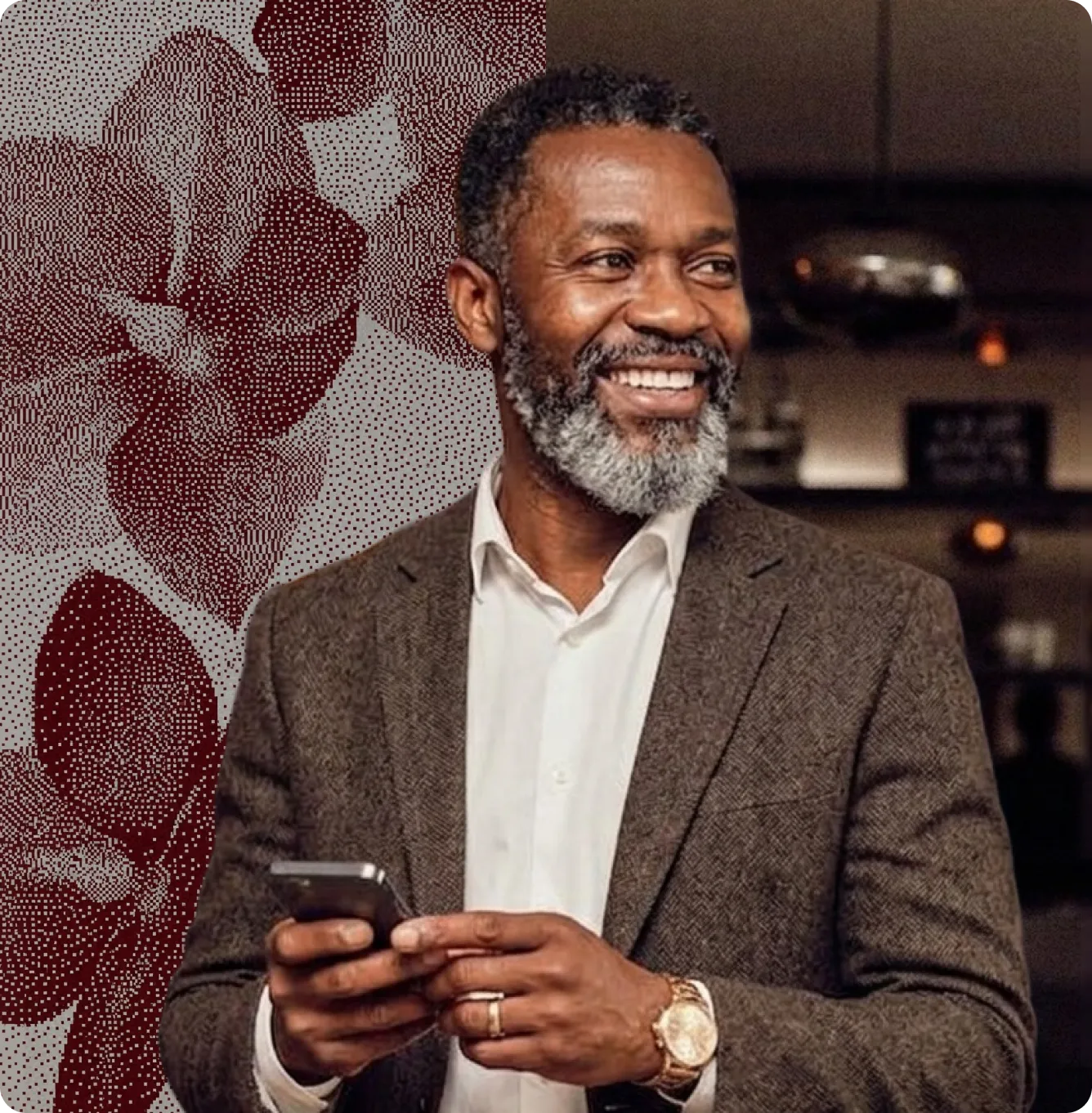 Homme souriant avec barbe grise portant un costume et tenant un smartphone en intérieur.