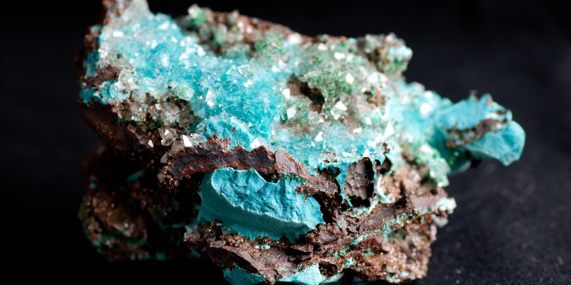 Nahaufnahme eines blaugrünen Kupferminerals, das auf dunkelbraunem Gestein wächst