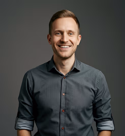 Smiling young man with rolled-up sleeves wearing a dark button-up shirt against a neutral background.