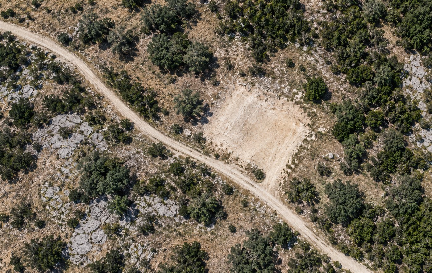 Aerial view of a cleared homesite beside a caliche road in Hill Country scrub