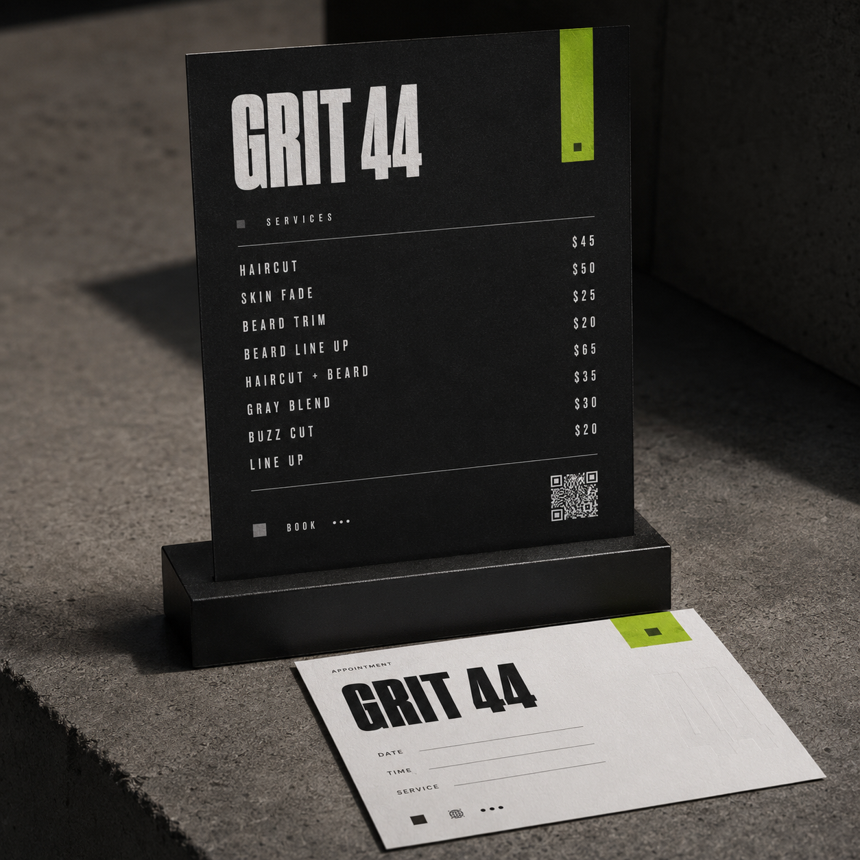 Black and white Grit 44 barber price list and appointment card on a gray surface.