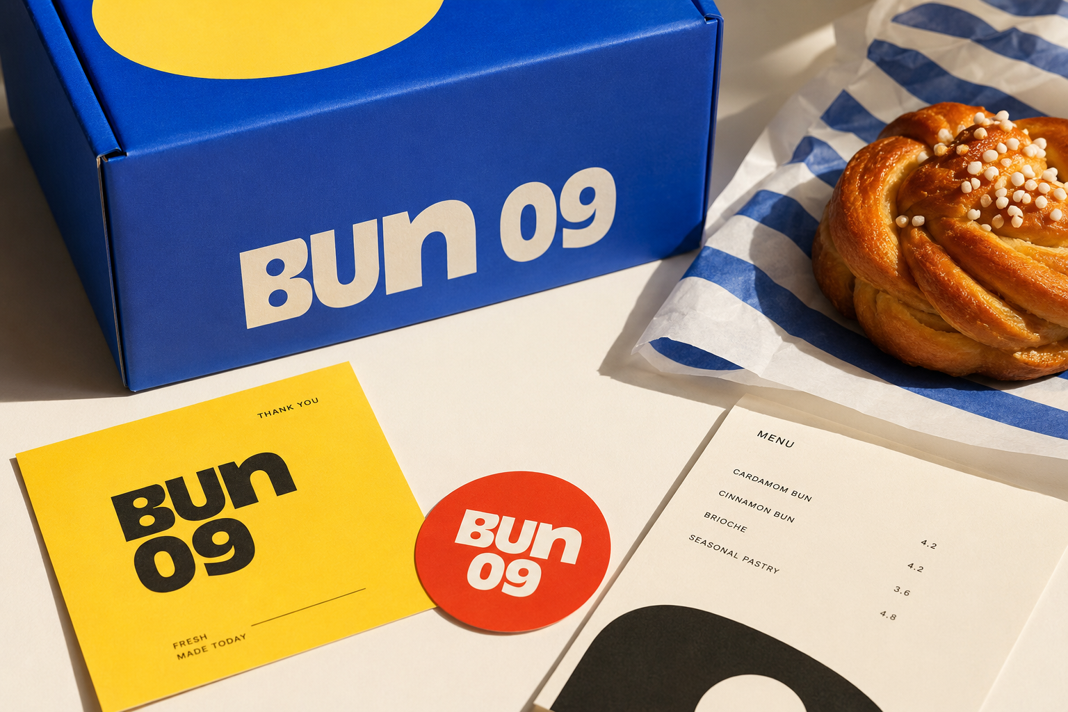 Blue Bun 09 box, a cinnamon bun on blue-striped paper, and branded cards with a menu listing pastries and prices.