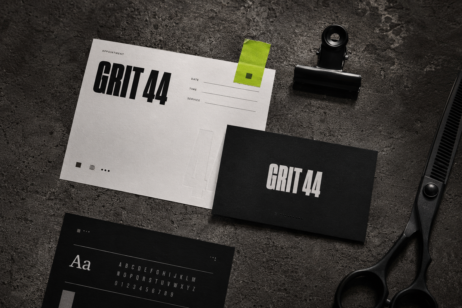 Black and white stationery with bold text GRIT 44 on dark textured surface with scissors and clip.
