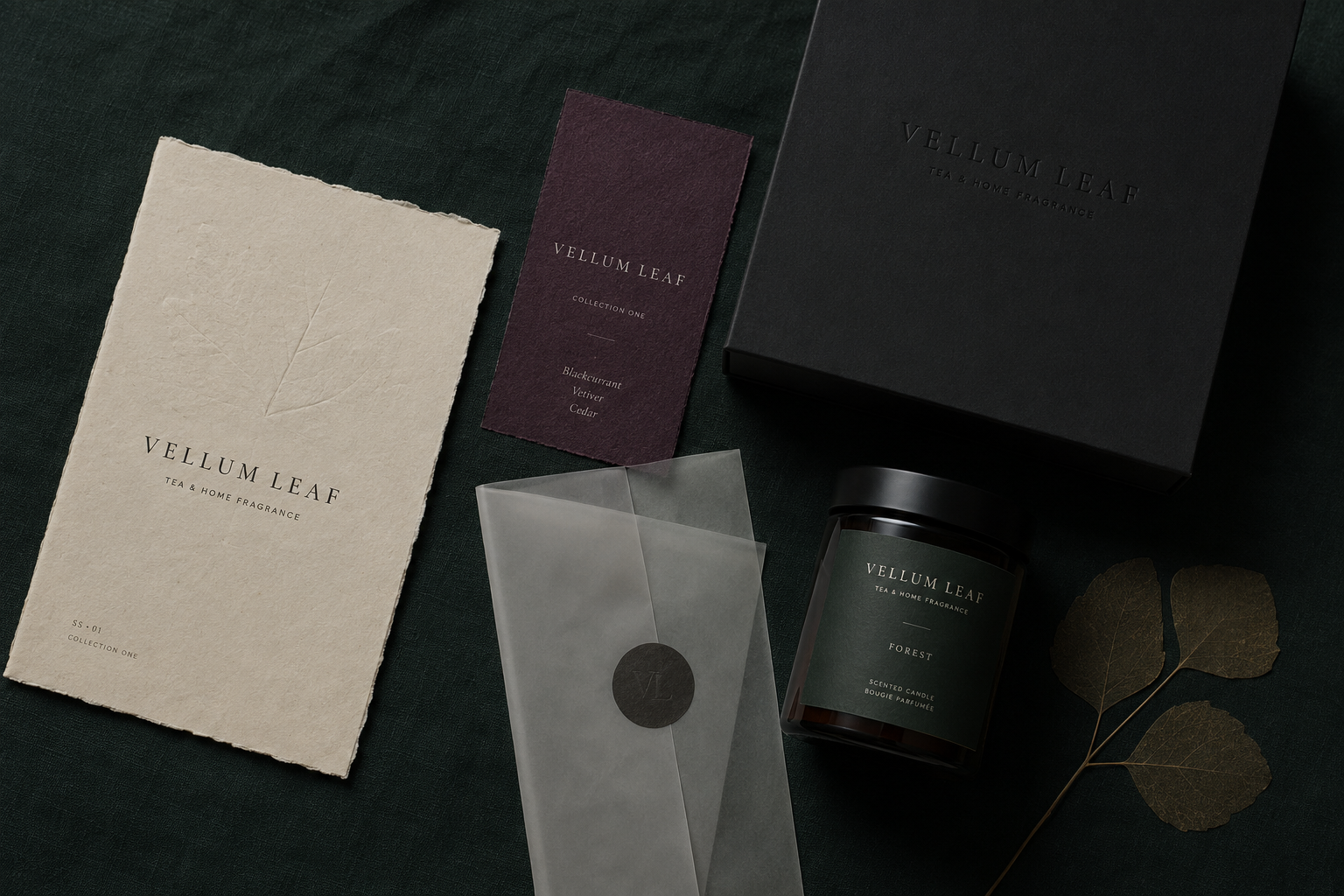 Vellum Leaf branded tea and home fragrance items including candle, cards, and packaging on dark fabric.